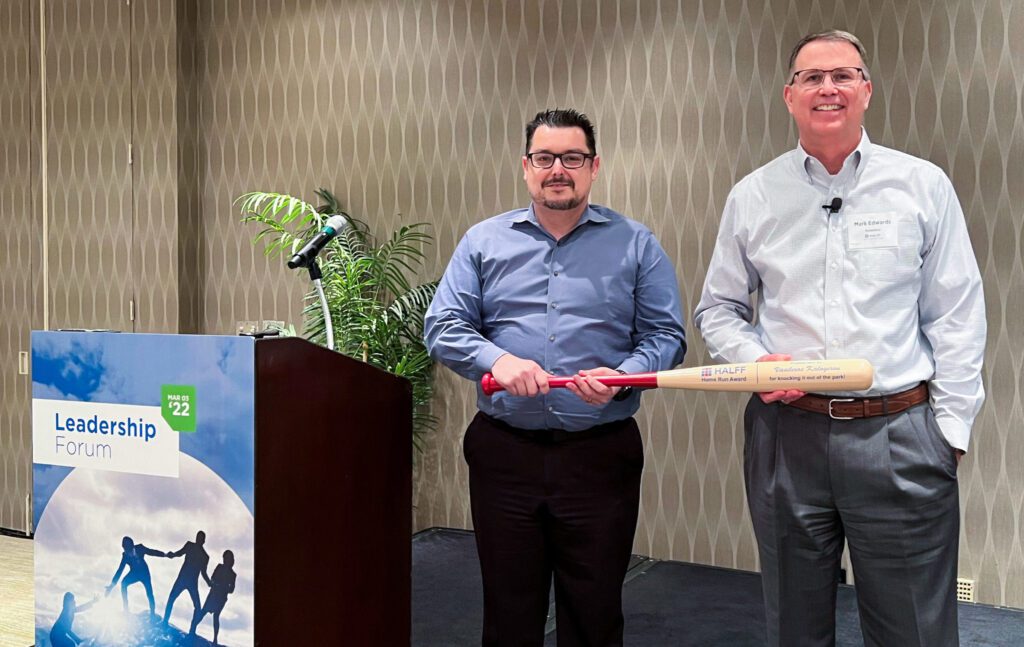 Two men on stage holding baseball bat award.